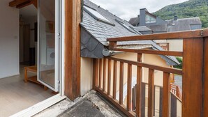 A balcony with a wooden railing, a sliding glass door leading to a room, and a view of neighboring houses and a hill in the background.