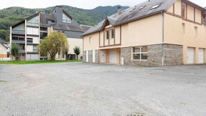 A building with a stone facade and a sloped roof, surrounded by a gravel parking area and a tree.