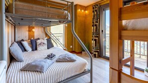 A bunk bed room with a wooden ladder, a window with curtains, and a small table with a cup and a book.