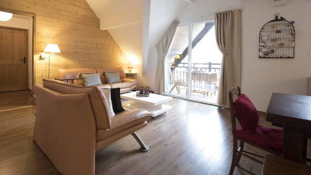 A spacious living room with a wooden sloped ceiling, a sofa set, a dining table, and a balcony with a birdcage. - Exceptional Duplex 10 pers, Jacuzzi, parking, Saint-Lary (Saint-Lary-Soulan)