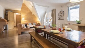 A modern loft-style room with a wooden dining table set for four, a sofa, and a bench. - Exceptional Duplex 10 pers, Jacuzzi, parking, Saint-Lary (Saint-Lary-Soulan)