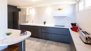 Una cocina moderna con encimera de mármol blanco, armarios oscuros y un refrigerador de acero inoxidable.