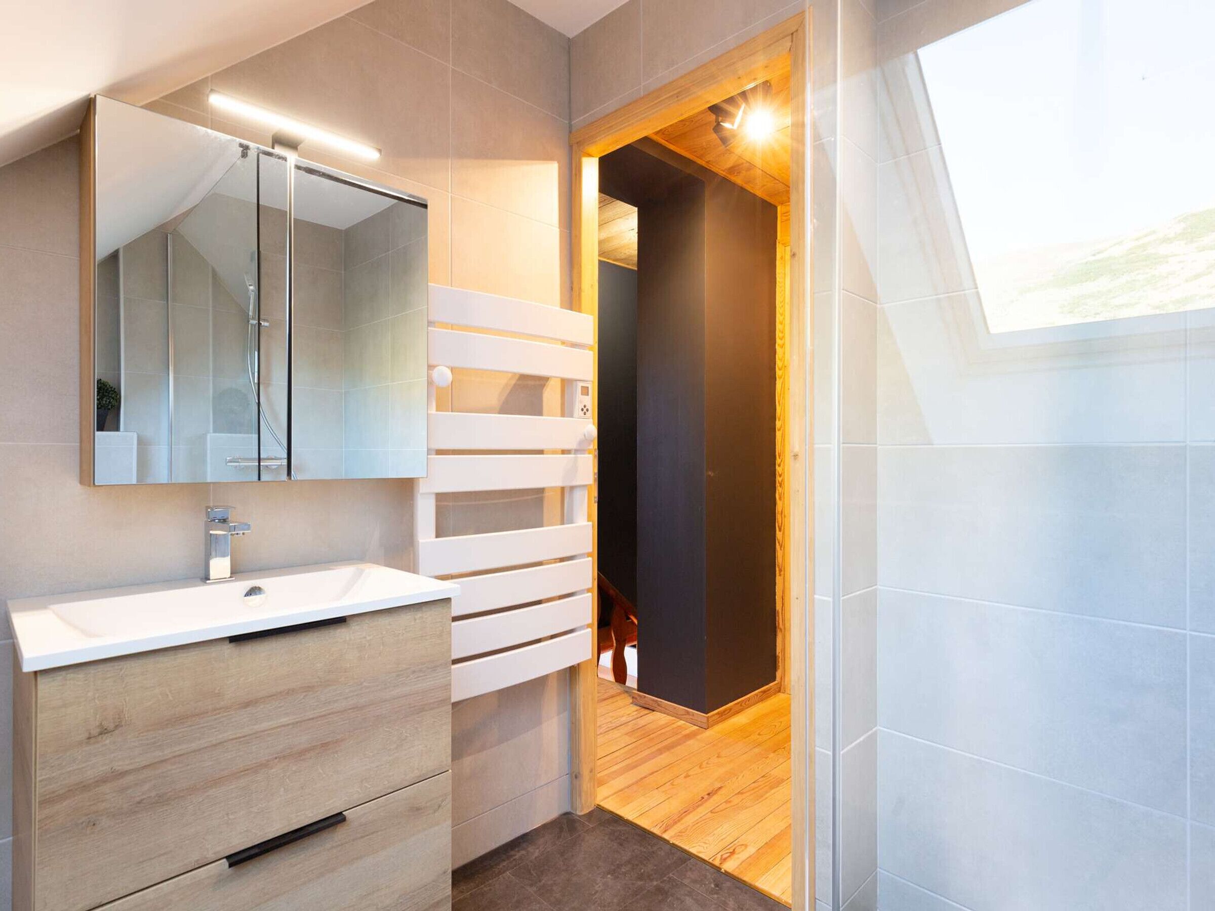 Un baño moderno con un espejo grande, tocador blanco y suelo de madera.