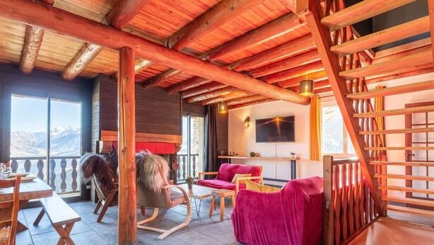 Un interior acogedor con vigas de madera, un sofá rojo, un sillón mecedor y un televisor en la pared.
