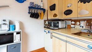 A compact kitchen with wooden cabinets, a blue hanging rack with pots, a white coffee machine, and a Galanz microwave.