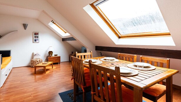 A room with a sloped ceiling, wooden flooring, a dining table with chairs, and skylights.