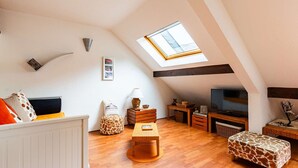 A cozy loft bedroom with a skylight, wooden furniture, and a television.