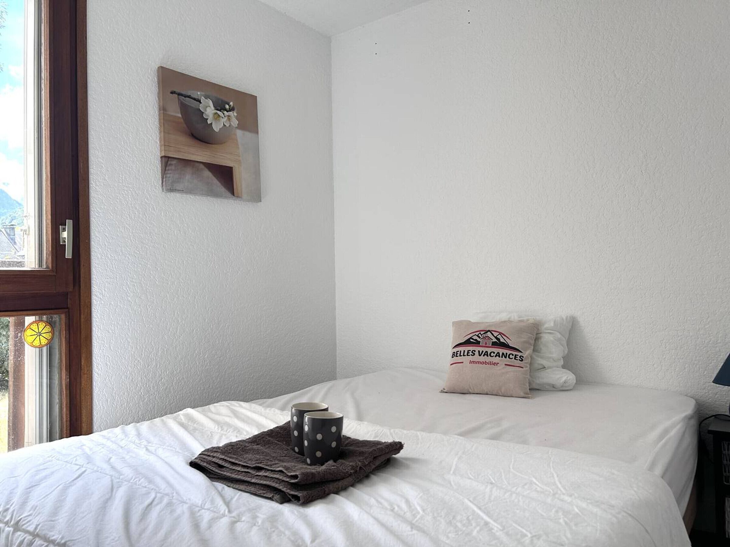 Une chambre à coucher avec un lit, des oreillers, une serviette et une tasse.