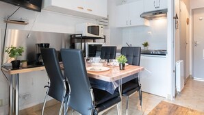 A compact kitchen with white cabinets, a microwave, and a stove. There is a dining table with chairs and a TV mounted on the wall. - Comfortable studio for 4 near cable car in Vielle-Aure (Vielle-Aure)