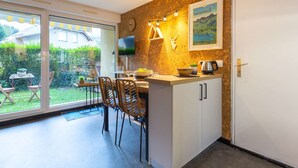 A modern kitchen with a stone backsplash, a dining area with wicker chairs, and a large window overlooking a garden. - Studio for 4, quiet area near center in Saint-Lary-Soulan (Saint-Lary-Soulan)