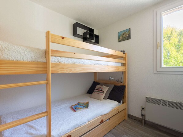 A bunk bed with a white fluffy mattress, a small desk with a lamp, and a window with a view of trees.