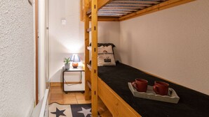 A small, narrow room with a bunk bed, a bedside table with a lamp, and a tray with two mugs. - Renovated apartment for 4, quiet, near Saint-Lary center (Saint-Lary-Soulan)