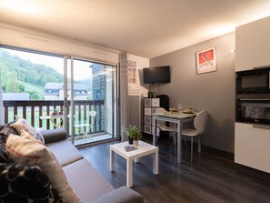 Ein modernes Wohnzimmer mit einer Couch, einem Esstisch mit Stühlen, einem an der Wand befestigten Fernseher und einer Küchenzeile mit einer Mikrowelle.