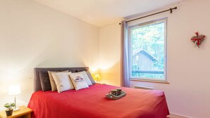 A bedroom with a bed, a nightstand, a window, and a view of a wooden cabin. - 4-person apartment with pool and parking in Vielle Aure (Vielle-Aure)