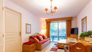 A cozy room with a sofa, a dining table with chairs, a TV, and a large window with curtains. - 4-person apartment with pool and parking in Vielle Aure (Vielle-Aure)