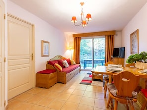 Una habitación acogedora con sofá, una mesa de comedor con sillas, televisión y un ventanal con cortinas.