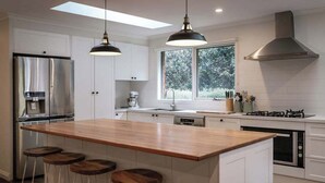 Een moderne keuken met een centraal eiland, barstoelen, een roestvrijstalen koelkast, een gasfornuis en een groot raam dat voor natuurlijk licht zorgt.