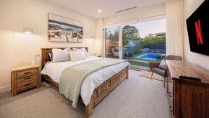 Een slaapkamer met een groot bed, een houten nachtkastje, een televisie en uitzicht op een zwembad.