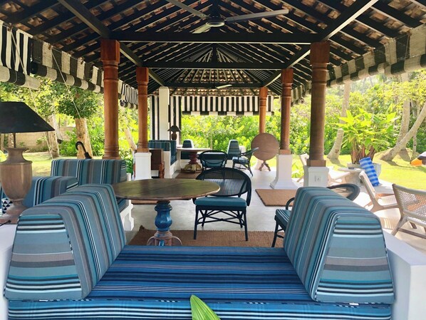 Un espace extérieur aménagé avec des meubles de jardin, comprenant des canapés à rayures et une table ronde, le tout entouré de verdure.