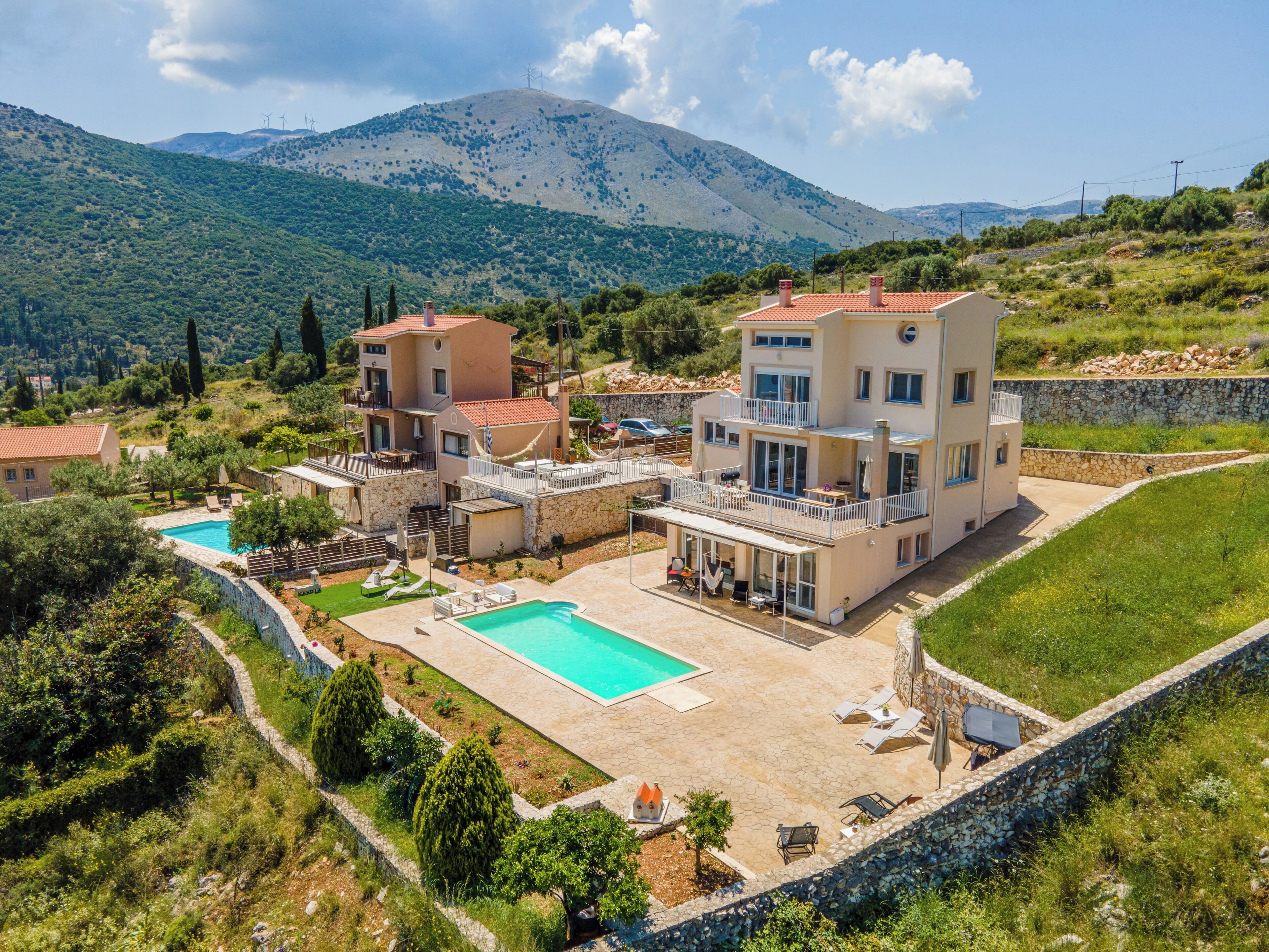 A multi-story villa with a swimming pool, outdoor seating, and a view of mountains.