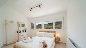 Un dormitorio con cama, mesitas de noche, armario, espejo y vistas al exterior.