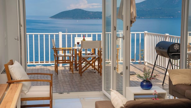 Un balcón con vista al mar, una mesa con sillas y una parrilla.