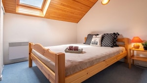 Une chambre confortable avec un plafond en pente, un lit avec un cadre en bois, une table de chevet avec une lampe et une fenêtre laissant entrer la lumière naturelle.