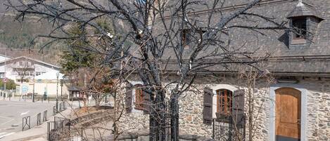 A stone building with a steep roof, a wooden door, and a metal fence.