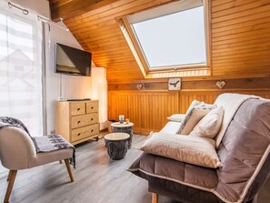 Una habitación acogedora con techo de madera, un televisor en la pared, un sofá, una silla y una mesita redonda.