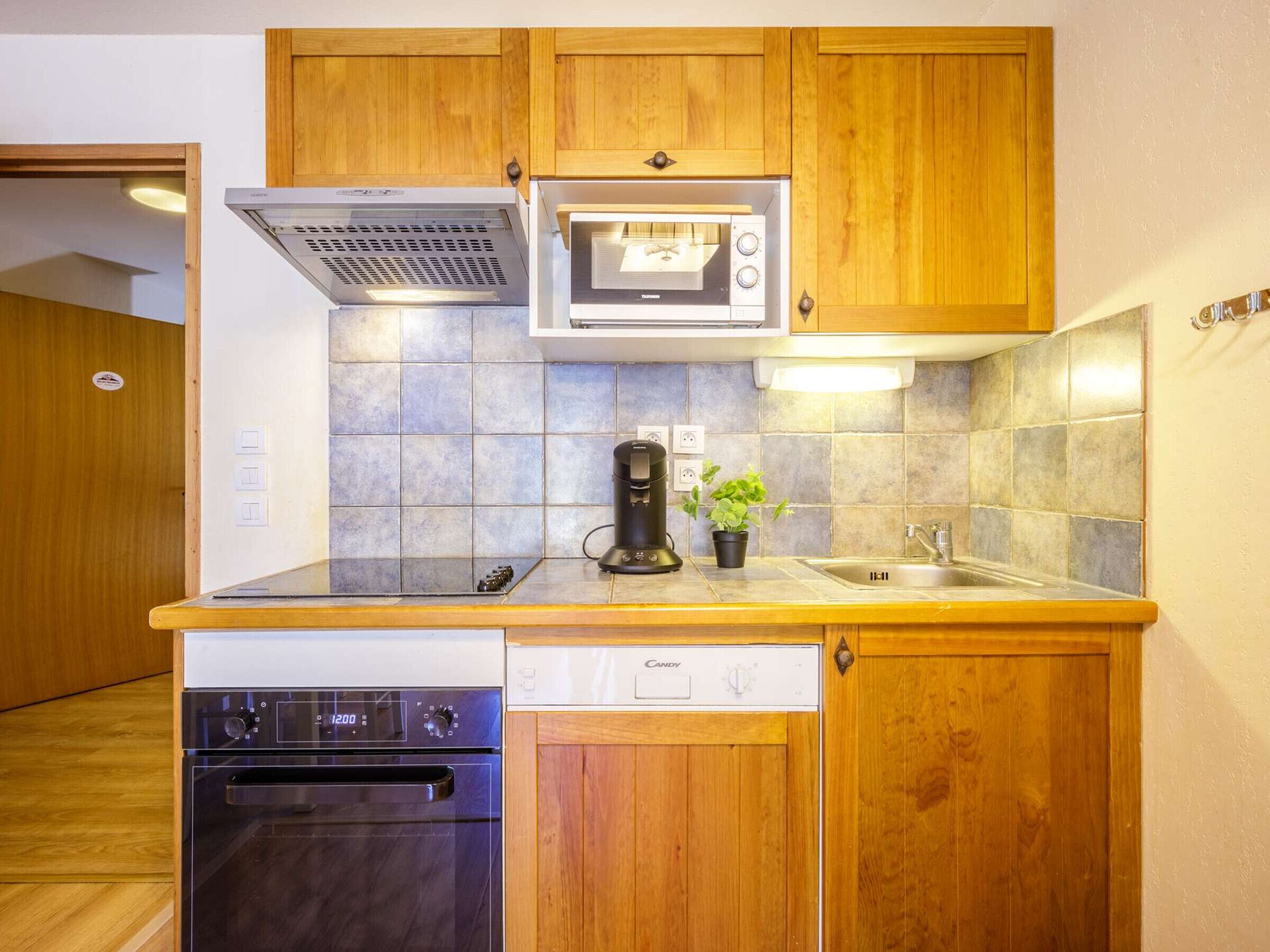 A compact kitchen with wooden cabinets, a built-in microwave, a coffee maker, and a dishwasher.
