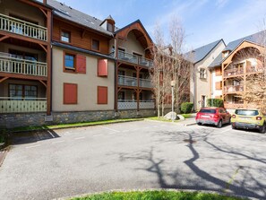 A multi-story building with balconies, a stone facade, and a parking area with cars. - Duplex Apartment for 8 with Pool and Sauna in City Center (Saint-Lary-Soulan)