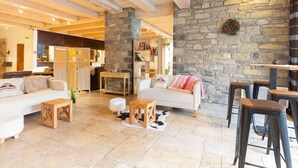 A cozy interior with a stone wall, wooden beams, a white sofa, and a bar area. - Duplex Apartment for 8 with Pool and Sauna in City Center (Saint-Lary-Soulan)
