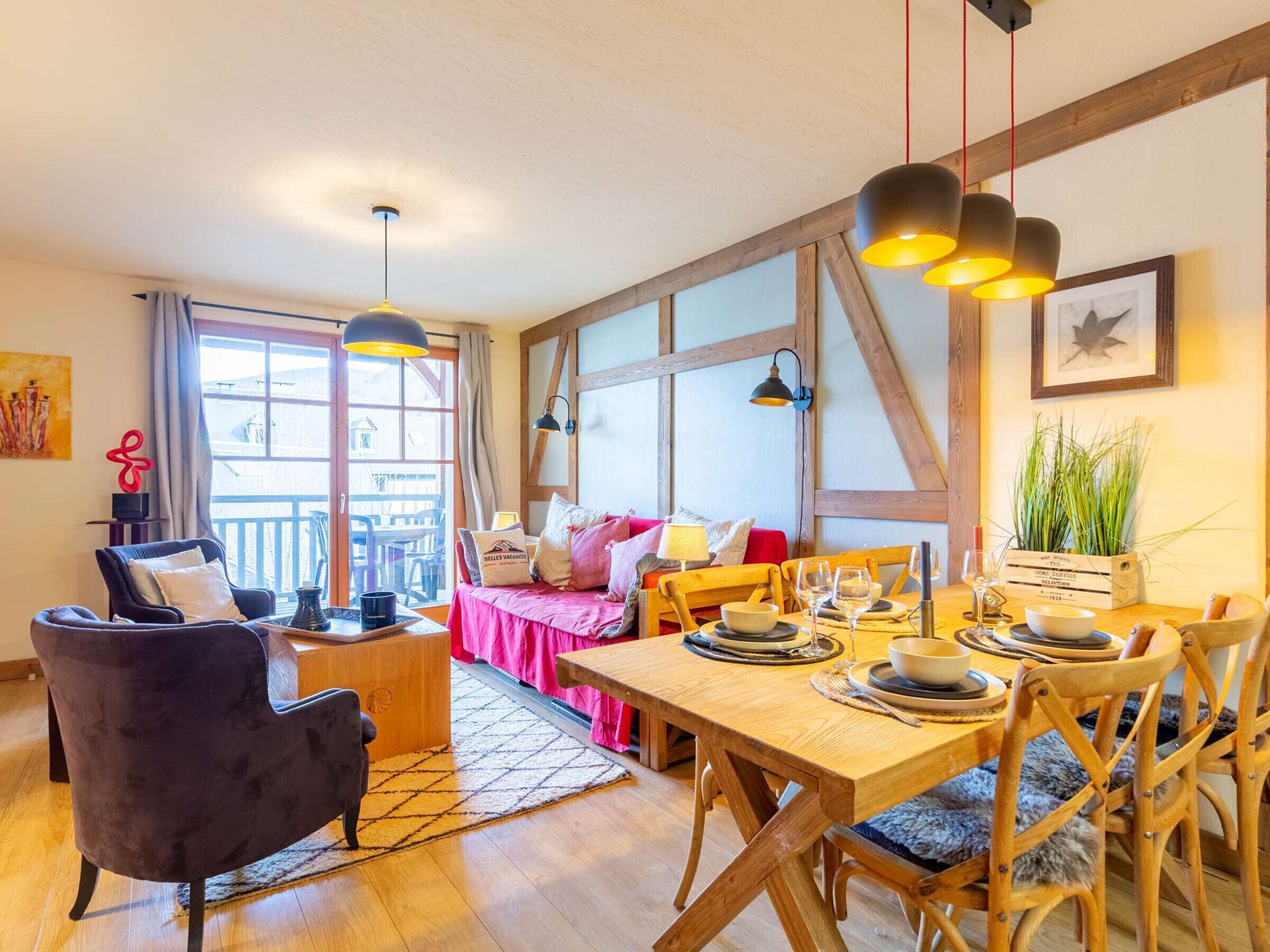 Et hyggeligt spiseområde med et træbord dækket til fire personer, en sofa med rosa betræk og udsigt udendørs gennem store vinduer.