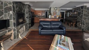 Un salon avec une cheminée en pierre, un canapé en cuir noir et une table basse sur laquelle sont posés des livres.