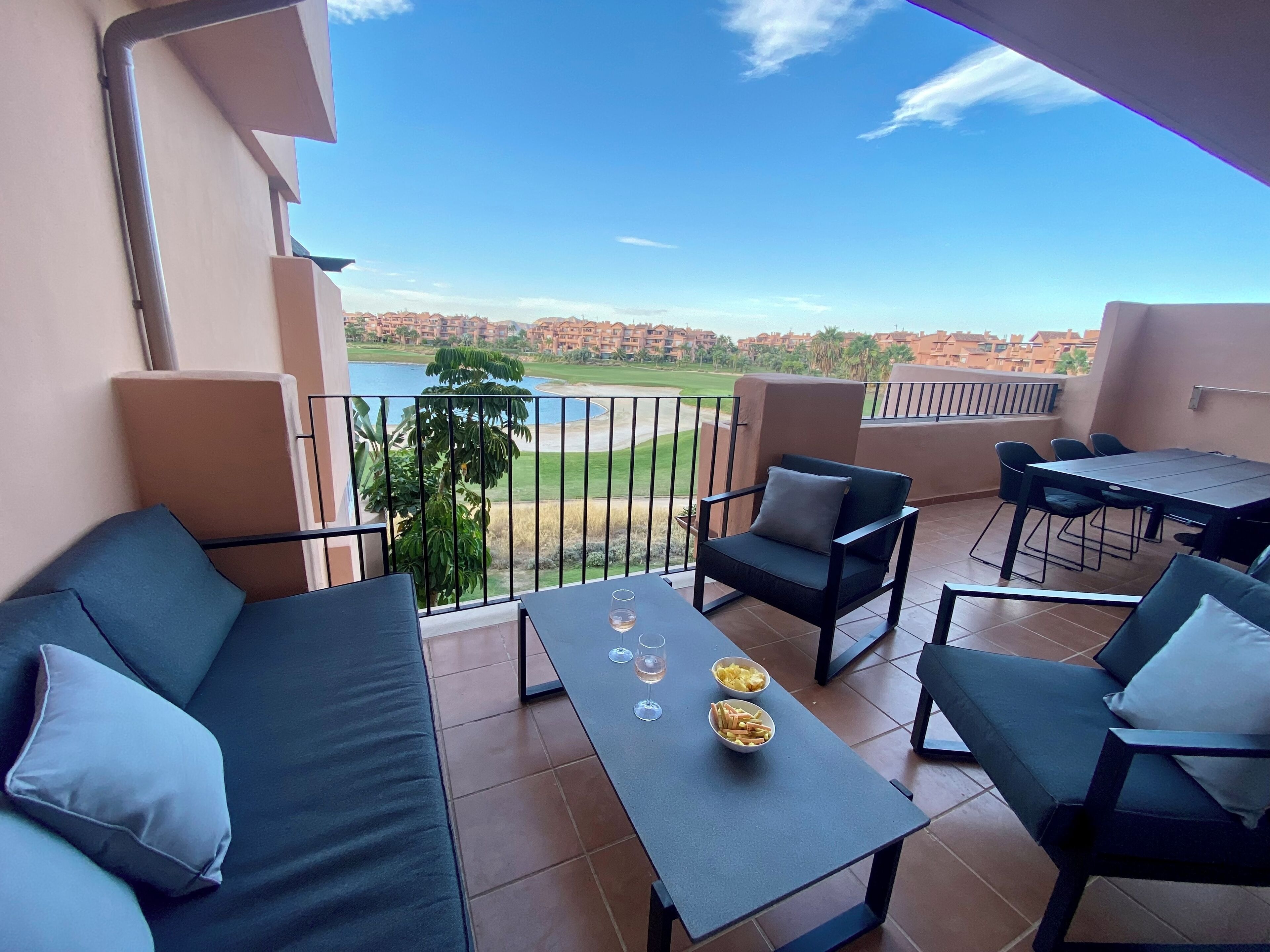 Een balkon met een bank, stoelen, een tafel en uitzicht op een golfbaan en gebouwen.