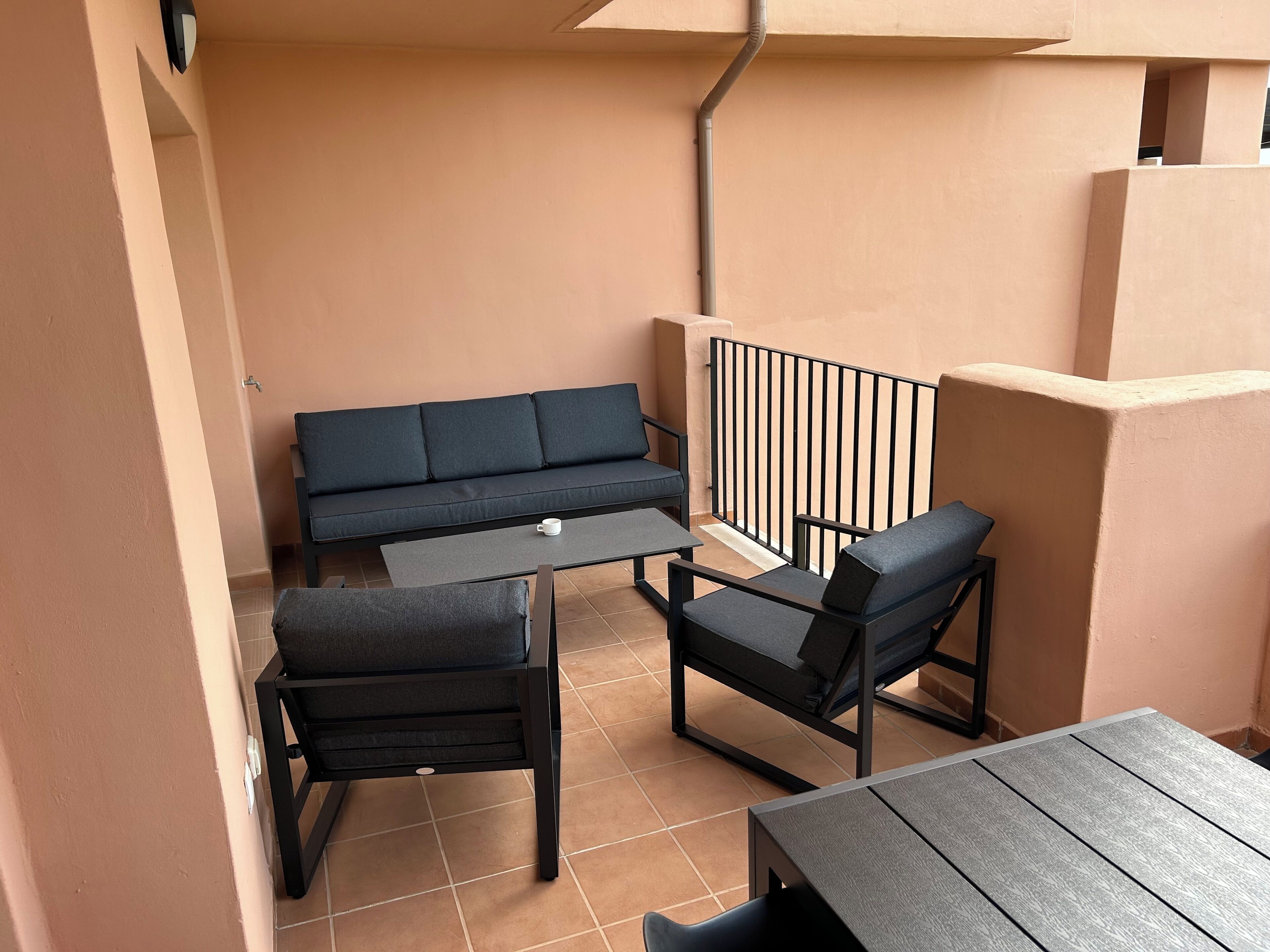 Een balkon met een bank, twee stoelen en een tafel.