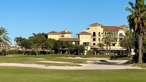 A golf course with a large building featuring multiple stories and a tiled roof.