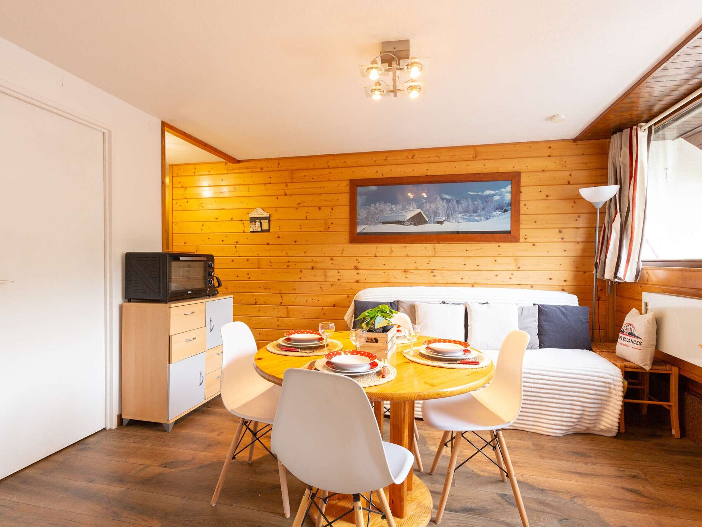 Un comedor acogedor con una mesa de madera dispuesta para cuatro personas, un microondas y un cuadro de un paisaje nevado en la pared.