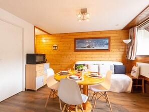 A cozy dining area with a wooden table set for four, a microwave, and a painting of a snowy landscape on the wall.