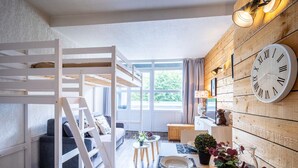 Habitació acollidora amb un llit superposat, zona de menjador amb un rellotge i una finestra gran.