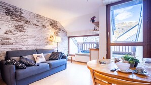 Un salón acogedor con un sofá azul, una mesa de comedor de madera y un gran ventanal con vistas a un balcón.