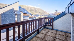 Un balcón con baranda de madera que da a una zona residencial con casas y montañas al fondo.