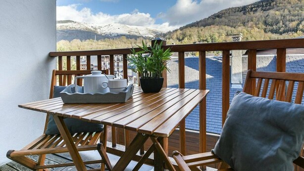 A wooden deck with a table and chairs, a potted plant, and a view of a mountainous landscape.