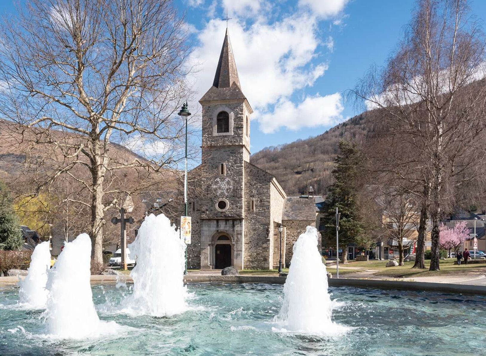 Una iglesia con una aguja, una fuente en primer plano, y un cartel con indicaciones.