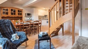 A spacious loft with a wooden staircase, a cozy seating area with a plush chair, and a kitchen with modern appliances.