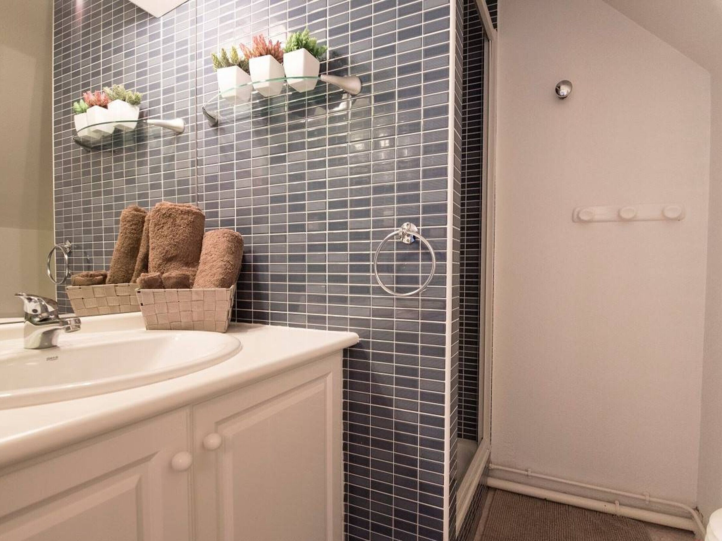A bathroom with a white sink, a mirror, a towel rack with towels, and a small plant shelf.