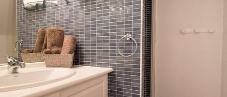 A bathroom with a white sink, a mirror, a towel rack with towels, and a small plant shelf.