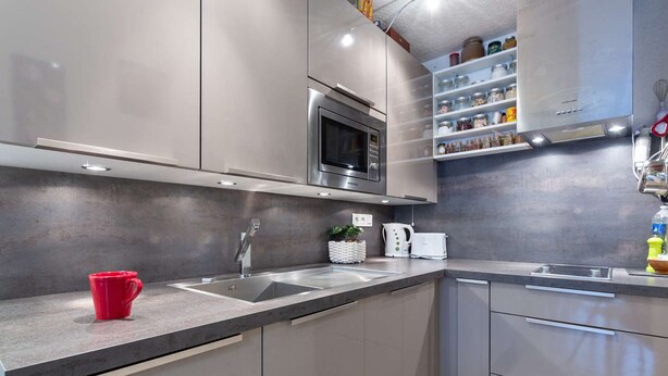 Une cuisine moderne avec des meubles gris, un four à micro-ondes en acier inoxydable, un four encastré et une étagère remplie de bocaux.