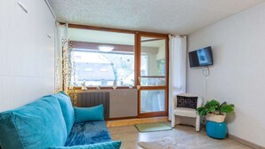 Un salon avec un canapé de couleur turquoise, un petit fauteuil blanc, un téléviseur fixé au mur et une plante en pot.