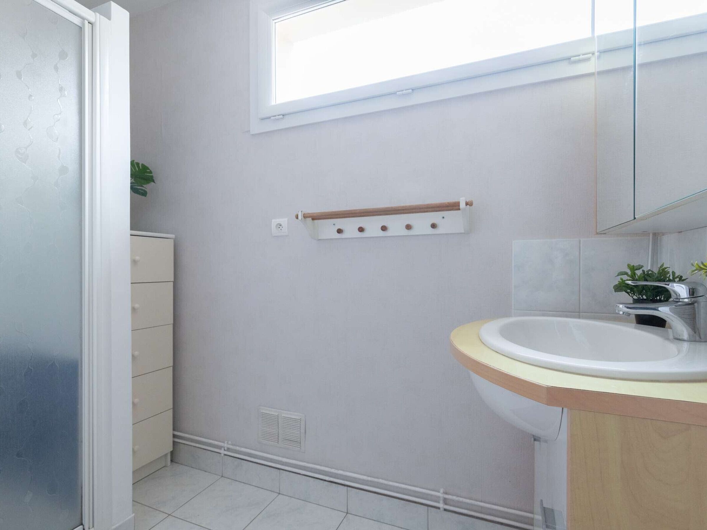 A bathroom with a white sink, a wooden countertop, a mirror, and a window above the sink.